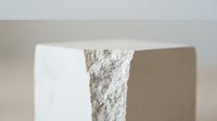 Minimalist white geometric sculpture with rough textured surface casting soft shadows on neutral background for modern interior design concepts.