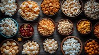 Variety of fresh popcorn flavors in wooden bowls on dark background, including caramel, cheese, and classic butter styles arranged in flat lay composition.