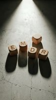Wooden letter blocks spelling EMDR under dramatic spotlight on cracked concrete floor creating long shadows for therapy and mental health concepts.