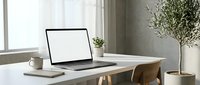 Modern minimalist home office workspace with open laptop displaying blank white screen on wooden desk near window with natural light and potted plant.