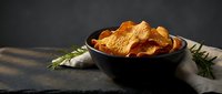 Crispy golden potato chips in dark bowl with fresh rosemary herbs on rustic wooden table for snack food packaging and culinary marketing materials.