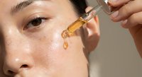 Young Asian woman applying facial serum with dropper for skincare routine and beauty treatment on glowing skin.