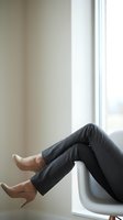 Professional woman legs in gray trousers and nude heels sitting by window in modern office interior for business and workplace concepts.