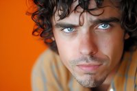 Handsome young man with curly hair and blue eyes looking at camera against vibrant orange background for lifestyle and portrait photography projects.