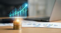 Golden coins stack with glowing digital growth chart hologram on wooden desk near laptop, symbolizing financial success and investment profits.