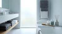 Modern minimalist bathroom interior with marble surfaces, floating vanity, bathtub and natural light from large window creating serene spa atmosphere.