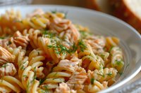 Delicious salmon pasta salad with spiral noodles and fresh herbs in white bowl, perfect for lunch meals and healthy dining recipes.
