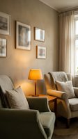 Cozy modern living room corner with comfortable armchairs, warm table lamp lighting, framed wall art and neutral beige color scheme for home decor.
