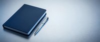Closed navy notebook with pen on white surface, minimalist workspace setup for business, education, planning, writing, and office organization concepts.