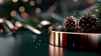 Pine cones and gold ribbon on metallic surface with bokeh lights and evergreen branches create festive holiday atmosphere against dark background.