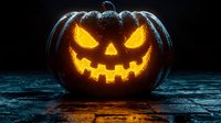 Glowing carved pumpkin with scary face illuminated from within on dark wooden surface. Orange light creates spooky Halloween atmosphere against black background.