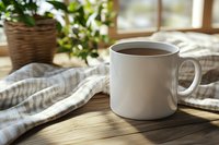 White ceramic mug filled with hot coffee on wooden table with striped linen napkin and potted plant, morning sunlight streaming through window creates cozy atmosphere.