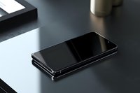 Modern black smartphone with glossy screen lying on dark surface in minimalist workspace setting with natural lighting and soft shadows.