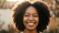 Happy African American woman with natural curly hair smiling outdoors in warm golden sunlight for lifestyle and wellness content.
