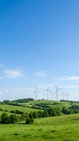 Wind turbines on rolling green hills under clear blue sky with white clouds, representing renewable energy and sustainable power generation for environmental and industrial applications.
