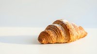 Fresh golden croissant with flaky layers on clean white surface, bakery pastry for breakfast menu design and culinary marketing materials.