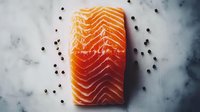 Fresh raw salmon fillet with distinctive marbling pattern on marble surface, garnished with scattered black peppercorns, captured in moody lighting.