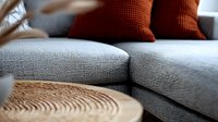 Modern living room interior with gray textured sofa, wooden round coffee table and deep red decorative pillows creating cozy contemporary home atmosphere.