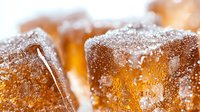 Macro shot of amber-colored sugar crystals on caramel candy cubes dusted with powdered sugar, creating a luxurious sweet texture for food and confectionery designs.