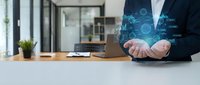 Professional businessman in dark suit displaying holographic cloud computing icons and data visualization in modern office workspace with laptop and plants.