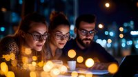 Young diverse professionals working late at office with laptop and coffee, illuminated by warm bokeh lights in modern urban setting. Teamwork and collaboration concept.