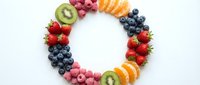 Fresh colorful fruits arranged in circular frame with strawberries, blueberries, raspberries, kiwi and orange slices on white background for healthy eating.