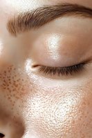 Close-up of glowing skin with natural freckles and closed eye showing long eyelashes and groomed eyebrow, highlighting dewy complexion and facial features.