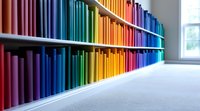 Colorful books arranged in rainbow spectrum order on library shelves create vibrant gradient display, modern minimalist interior design element for education spaces.