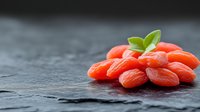 Fresh goji berries with green leaves on dark slate surface for healthy superfood nutrition and wellness concepts.