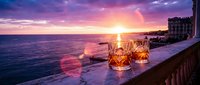 Romantic sunset cocktails on Mediterranean terrace overlooking ocean with crystal glasses and golden hour lighting for luxury travel and dining concepts.