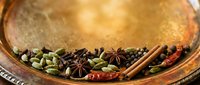 Assorted spices including star anise, cardamom, cinnamon sticks, and cloves arranged in a copper bowl for cooking and culinary use.