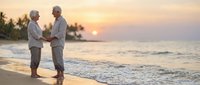 Two senior men in white shirts holding hands on tropical beach at golden sunset, romantic couple enjoying peaceful moment by ocean waves.