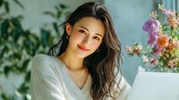 Young Asian woman smiling warmly at camera in bright modern home office with laptop and flowers, remote work lifestyle concept for business content.