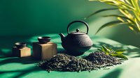 Traditional cast iron teapot with loose green tea leaves scattered on dark surface against emerald background with palm leaves creating zen atmosphere for tea ceremony.
