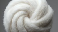 White fluffy wool roving twisted into spiral shape, soft natural fiber material for crafts, felting, and textile arts projects.
