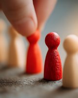 Fingers selecting red wooden pawn figure among other game pieces, symbolizing leadership choice, team selection, or strategic decision making.