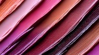 Diagonal stripes of creamy makeup texture in pink, burgundy and coral shades create abstract background pattern with soft gradient and luxurious satin finish.