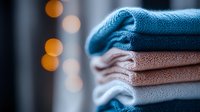 Neatly folded stack of cozy knitted sweaters in blue, pink and white tones with soft bokeh lights in background, creating warm domestic atmosphere.