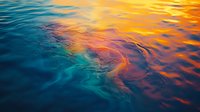 Vibrant sunset reflection on calm ocean water surface with golden orange and turquoise blue ripples creating abstract natural patterns for backgrounds.