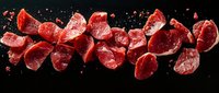 Fresh raw beef chunks arranged in line with water drops and splashes on black background, dramatic food photography for restaurant menu and culinary design.