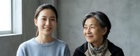 Young Asian woman and elderly Asian grandmother smiling together in modern home interior with natural window light for family bonding concepts.