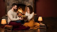 Young Caucasian couple enjoying cozy evening by fireplace, reading books together in warm living room with soft lighting and comfortable blankets.