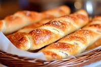 Fresh baked pretzel breadsticks with golden brown crust and salt sprinkled on top, arranged in woven basket with white paper liner. Artisanal bakery food.