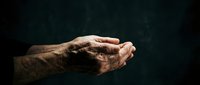 Elderly hands clasped together in prayer or contemplation against dark background, showing wrinkles and age spots with dramatic lighting for spiritual concepts.