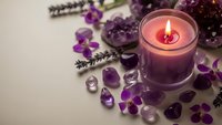 Purple candle burning surrounded by amethyst crystals, lavender flowers and gemstones creating peaceful spa atmosphere for meditation and relaxation.