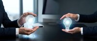 Two business professionals in suits exchanging glowing light bulb holograms, symbolizing idea sharing, innovation, and creative collaboration in modern workspace.