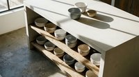 Wooden shelving unit with white countertop displaying organized collection of ceramic bowls and vessels in neutral tones for kitchen storage and display.