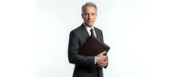 Middle-aged Caucasian male professional businessman wearing dark suit and tie, holding black folder or tablet, isolated on white background for corporate and business use.