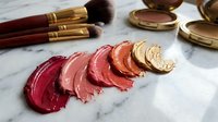 Luxury makeup collection with colorful lipstick swatches and golden cosmetic brushes on marble surface for beauty and fashion applications.