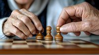 Senior hands moving wooden chess pawns on board during game, close-up view showing aged skin texture and strategic gameplay moment.